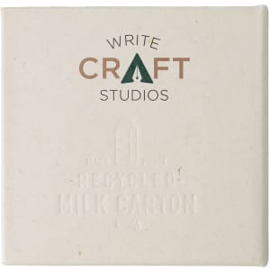 A square, off-white notepad with subtle embossed text, featuring a logo and made from recycled materials.