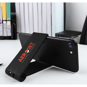A black phone stand with a logo, positioned upright on a desk beside office supplies.