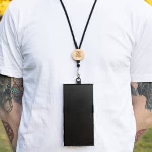 A black neck lanyard with a wooden attachment, holding a smartphone against a plain white shirt.