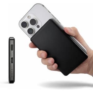 A black power bank held in one hand, with a smartphone partially visible in the background.