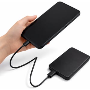 A black solid state power bank with a charging cable connected, held in a hand.