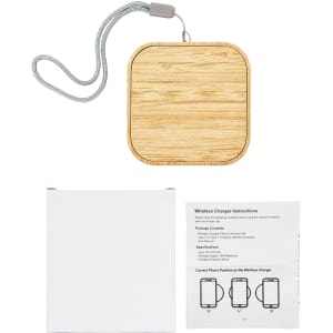 A square wireless charger with a bamboo finish and a grey strap, alongside a white box and instruction manual.