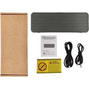 A black speaker with a mesh cover, accompanied by charging cables, a manual, and packaging.
