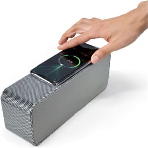 A silver speaker with a textured surface and a smartphone placed on top for charging.