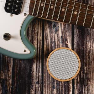 A Bluetooth speaker featuring a bamboo exterior, positioned beside an electric guitar on a wooden surface.