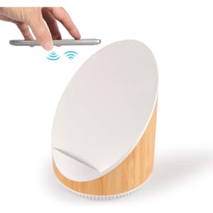 A wireless charger and speaker with a white top and bamboo base. A smartphone is held above the charger.