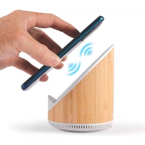 A wireless charger and speaker with a bamboo design, showing a hand placing a phone atop the device.
