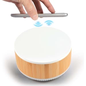 A wireless charger and speaker with a white top and bamboo base, featuring a hand holding a smartphone above it.