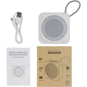 A white wireless speaker with a round mesh speaker area, USB cable, instruction manual, and brown packaging.