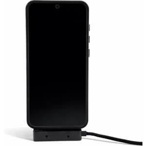 A black smartphone set on a stand with a charging cable connected, featuring a logo on the cable.