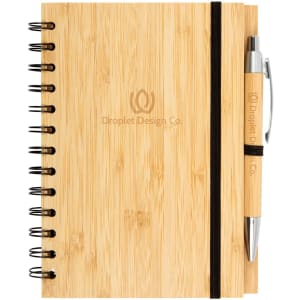 A bamboo notebook with a spiral binding and a matching pen, featuring a logo on the front.