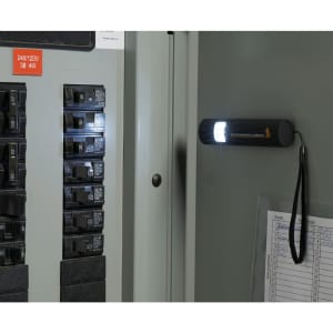 A black mini grip slim LED flashlight attached to a metal surface, illuminating electrical circuit breakers.