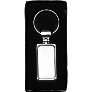 A silver metal keyring with a rectangular pendant, packaged in a black box.