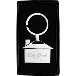 A house-shaped metal keyring in silver, displayed in a black box with a logo. It's sleek and stylish.