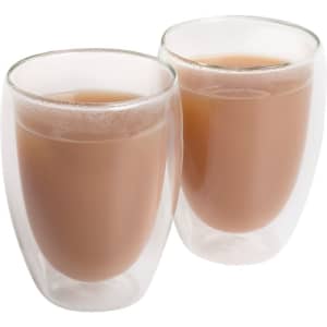 Two double-walled, transparent glass cups filled with light brown liquid. The cups have a sleek design and a logo.