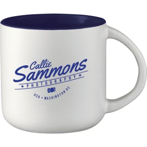 A ceramic coffee mug with a white body and navy blue interior, featuring a logo on one side.