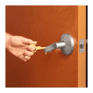 A yellow no-contact keychain is being used to open a door handle, featuring a metallic finish.