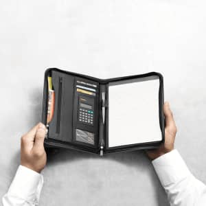 A black portfolio opened to reveal a notepad, calculator, pen, and card slots, held in hands.