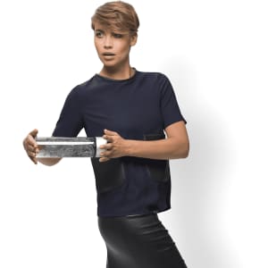 A drink bottle with a sleek silver design, featuring a logo, held by a person in a stylish outfit.