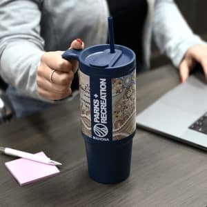 A drink bottle featuring a blue body and decorative patterned sleeve, with a handle and straw, resting on a table.