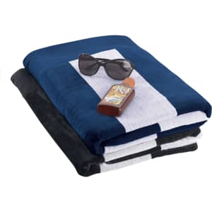 A stack of beach towels in navy blue, black, and grey, with sunglasses and a bottle of sunscreen on top.