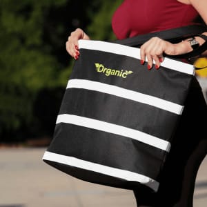 A black and white insulated cooler bag with a logo, held by a person outdoors.