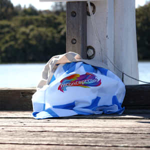A blue and white Palm Cove Beach Towel draped over a wooden pier, with a logo partially visible.