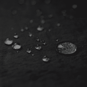 A close-up of water droplets on a textured black surface, showcasing various sizes and reflections.