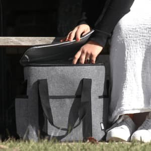 A drink bottle cooler bag in grey felt with black straps, being opened to reveal its interior.