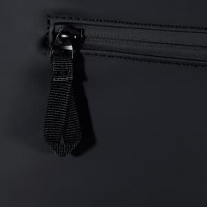 A close-up of a black backpack zipper with a fabric pull tab. The material appears water-resistant.