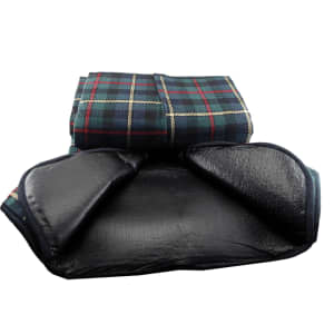 A picnic rug with a checkered pattern in green and navy, featuring a black waterproof backing. It has a logo on the edge.