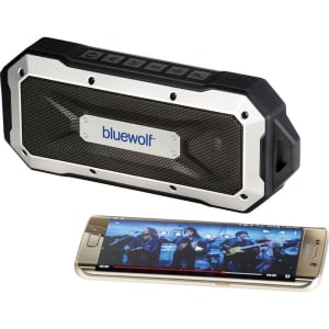 A black and silver waterproof Bluetooth speaker beside a smartphone displaying a music video. The speaker features a logo.
