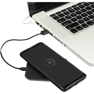 A wireless charging phone stand in black, with a smartphone on it, connected to a laptop by a charging cable.