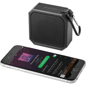 A black waterproof Bluetooth speaker with a textured mesh front and a carabiner, next to a smartphone displaying music.