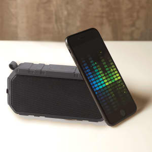 A grey outdoor waterproof Bluetooth speaker placed next to a smartphone displaying a visual equaliser.