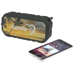 A black, outdoor waterproof Bluetooth speaker beside a smartphone displaying music controls, featuring a tropical background.