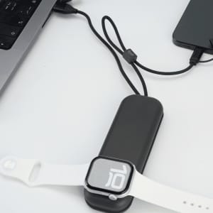 A black foldable charging cable with a wireless watch charger, connected to a laptop and a phone, next to a white watch.