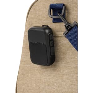 A black magnetic Bluetooth speaker attached to a tan bag strap. The speaker features buttons and a sleek design.