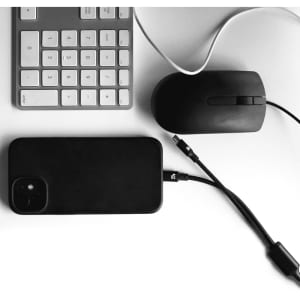 A black 4 in 1 fast charging data transfer cable next to a black phone, mouse, and keyboard on a white surface.