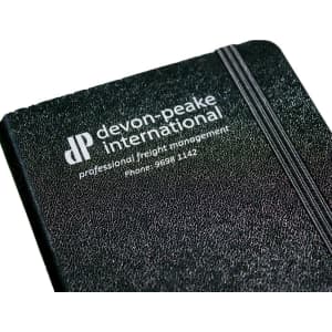 A black bound journal with a textured cover, featuring a logo and branding on the front.