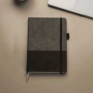 A5 Thermo notebook featuring recycled paper, with a textured grey and black cover, placed on a desk with a laptop.