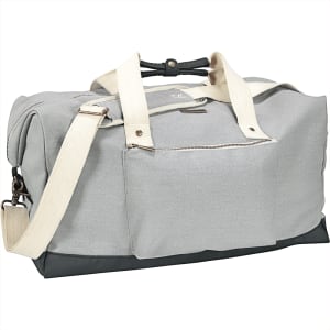 A grey cotton duffel bag with a black bottom, featuring fabric handles and a shoulder strap, along with a front zip pocket.