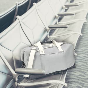 A grey duffel bag with white straps rests on a seating area, featuring a logo on the side.