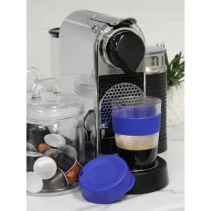 A drink bottle with a blue silicone band and lid, next to a coffee machine and coffee capsule containers.