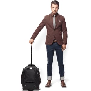 A man in a suit stands beside a black wheeled compu-backpack with a retractable handle.