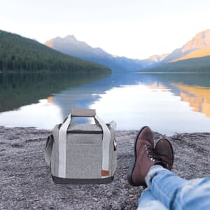A grey cooler bag with handles near a lake, surrounded by mountains and nature.