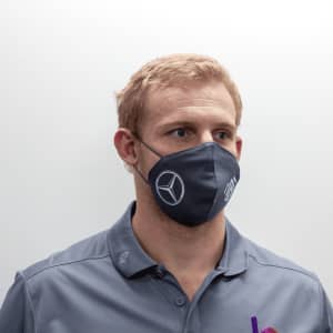 A grey face mask with a logo, worn by a person, featuring ear loops for a secure fit.