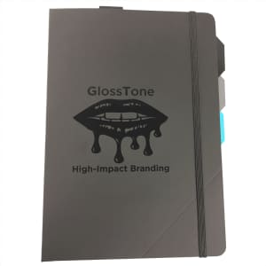 A black notebook with an elastic band closure and a logo featuring dripping lips, accented with colour tabs.