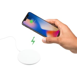 A hand holds a smartphone above a round, white wireless charging pad, with a charging symbol displayed.