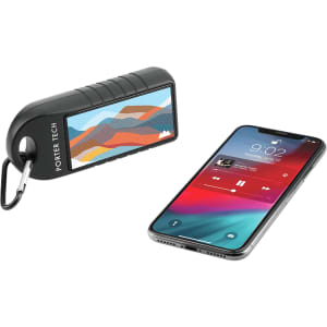 A black Bluetooth speaker with a mountain design beside a smartphone displaying music playback.